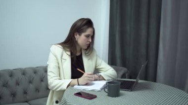 Dizüstü bilgisayarı olan bir kadın öğrenci evle ilgili notlar alıyor.