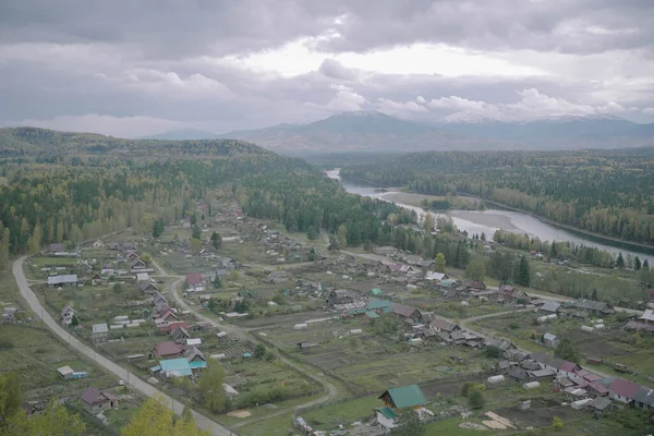 Nehir, evler ve tepeleri olan bir Rus köyü. Bulutlu gökyüzü, panoramik manzara