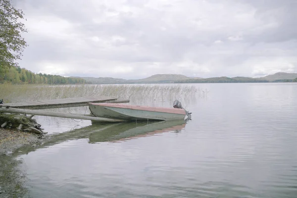 Nehirdeki eski tekne, sisli gökyüzünün altındaki dağ tepeleri.