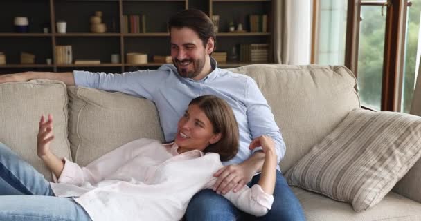 Молода пара закохалася розслабитися на дивані у вітальні — стокове відео