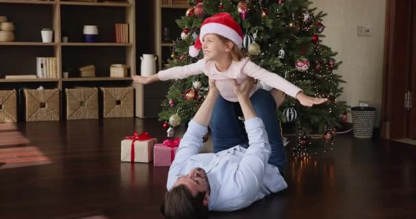 Papá se acuesta en el suelo sostiene a su hijita en brazos extendidos — Vídeo de stock