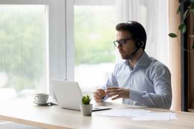 Kablosuz kulaklıklı kendine güvenen adam konuşuyor, dizüstü bilgisayar kullanıyor, internette sohbet ediyor.