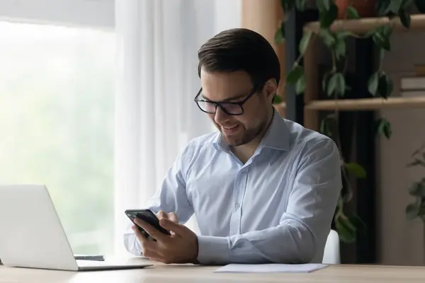 Hombre de negocios sonriente en gafas usando smartphone en el lugar de trabajo — Foto de Stock