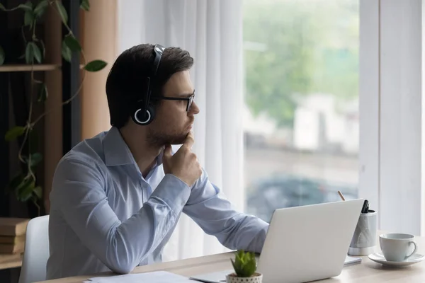 Thoughtful man in glasses and headphones looking in distance