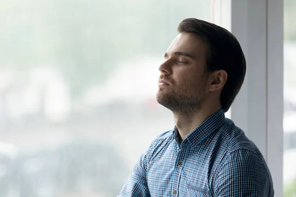 Primer plano hombre consciente con los ojos cerrados meditando cerca de la ventana — Foto de Stock