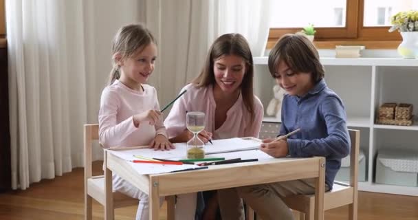 Feliz joven niñera pintar cuadros contra reloj de arena con niños — Vídeo de stock