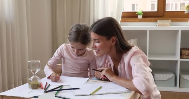 Девочка сидит за столом и рисует вместе со взрослой сестрой — стоковое видео