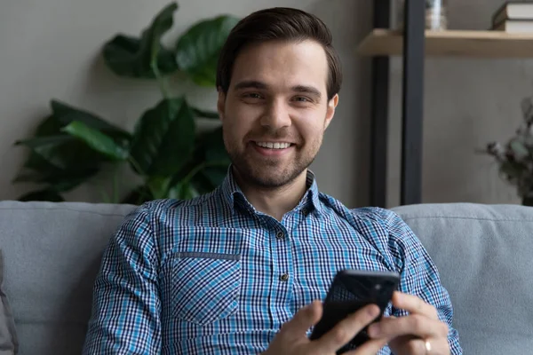 Testa ritratto sorridente uomo che tiene smartphone, seduto sul divano — Foto Stock