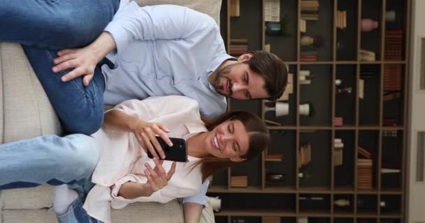 Pareja joven enamorada acurrucada en el sofá use smartphone — Vídeos de Stock