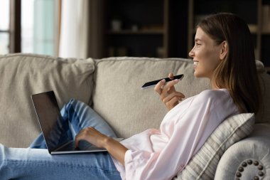 Happy young woman resting on soft cozy couch with gadgets clipart