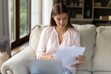 Odaklanmış genç bayan ev sahibi kağıt faturaları üzerinde çalışıyor.