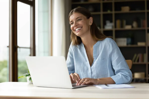 Happy young employee working at laptop, looking away, smiling — Stock Photo, Image