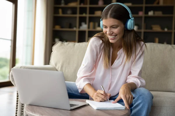Happy girl in big headphones writing down online lecture notes — Stock fotografie