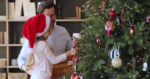 父亲和小女儿戴着圣诞帽子装饰杉树 — 图库视频影像