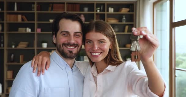 Возбужденная молодая супружеская пара обнимается, глядя на камеру с ключами — стоковое видео