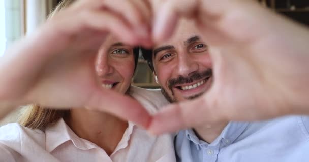 Couple amoureux regardant la caméra à travers le cœur des mains unies — Video