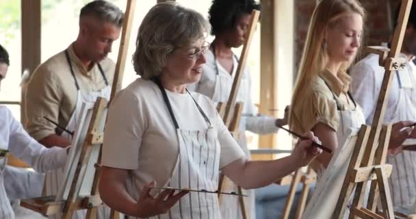 Pessoas diversas pintando com pincéis em cavaletes no estúdio de arte — Vídeo de Stock