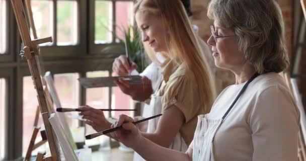 Starší žena maluje na stojan s jinými lidmi v dílně — Stock video