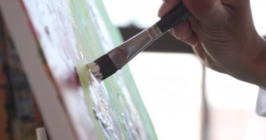 Yakından bir ressam elinde fırçayla tuvale resim çiziyor.