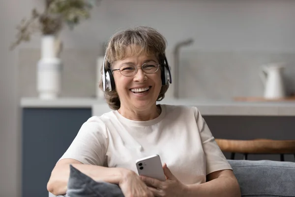 Glücklich lachende Frau mittleren Alters, die mit Kopfhörern Musik hört. — Stockfoto