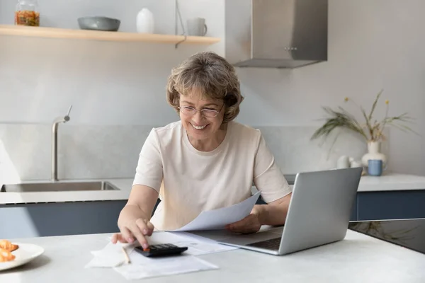 Glimlachende oudere gepensioneerde vrouw die huishoudelijke uitgaven berekent. — Stockfoto