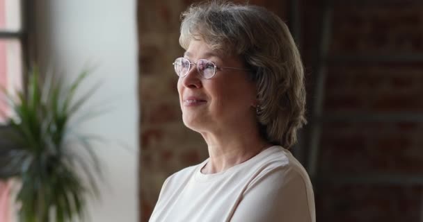 Γυναίκα 60 ετών με γυαλιά ονειρεύεται να στέκεται σε εσωτερικούς χώρους κοιτάζοντας την απόσταση — Αρχείο Βίντεο