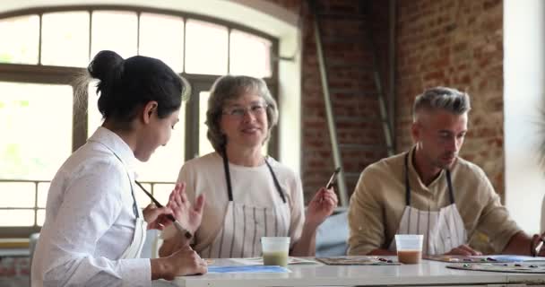 Grupo de personas diversas se sientan a la mesa pintando cuadros — Vídeos de Stock