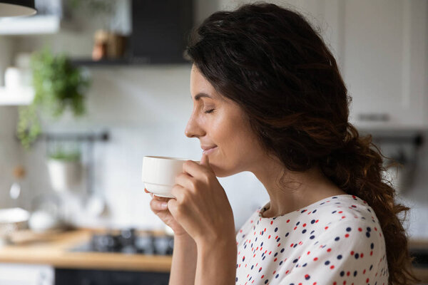Happy peaceful woman enjoying morning coffee in kitchen