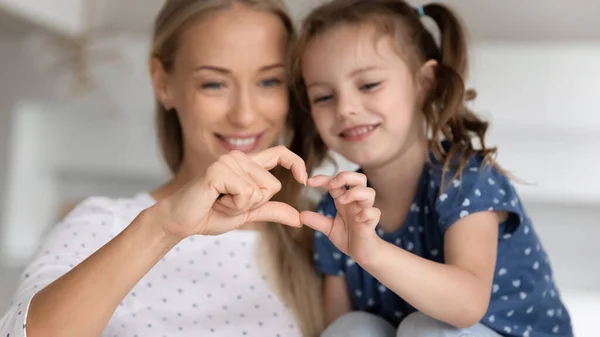 Leende ung mor och liten dotter visar hjärtat symbol. — Stockfoto