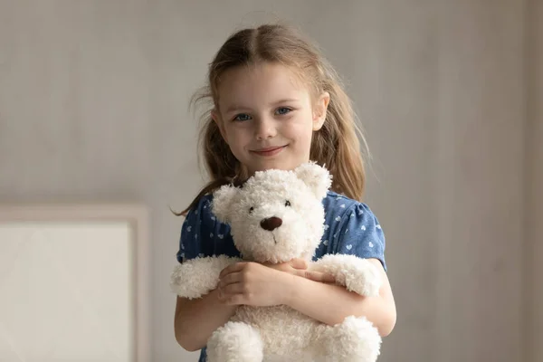 Portrait de petite fille souriante câlinant jouet pelucheux préféré. — Photo