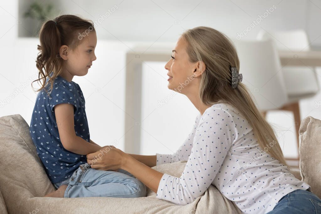Smiling young woman involved in sincere conversation with child daughter.