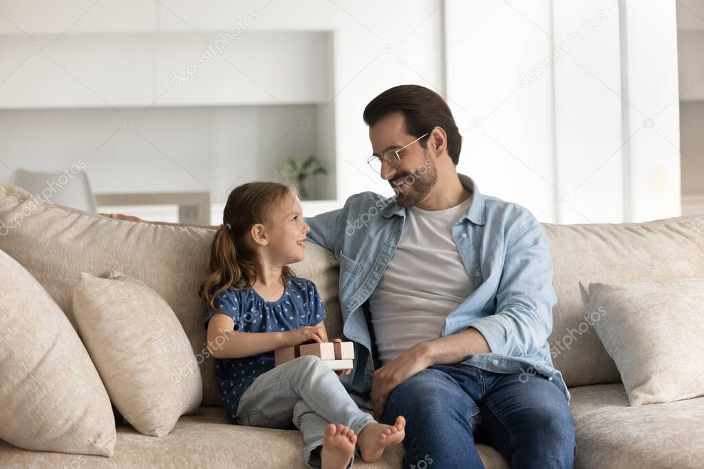 Happy little girl holding gift, sitting on sofa with dad.