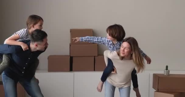 Despreocupada pareja joven padres sosteniendo en la espalda alegre niños pequeños. — Vídeos de Stock