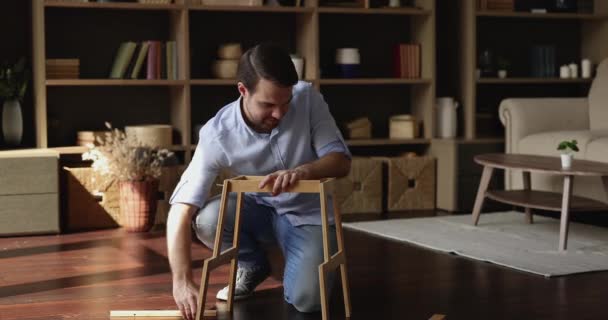 Опытный молодой человек собирает мебель из плоской упаковки дома — стоковое видео