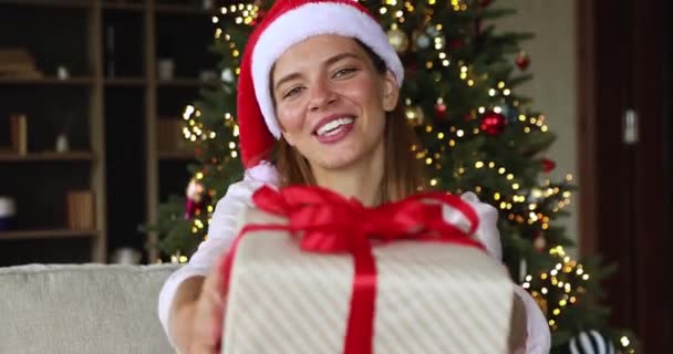 Девушка в шляпе Санта предлагает вам новогодний подарок — стоковое видео