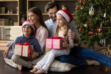 Mutlu bir aile paketli hediyelerle yerde oturuyor..
