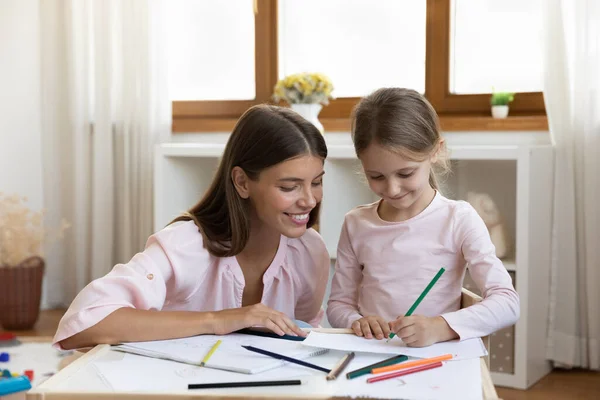 Lächelnde Millennial-Mutter zeichnet mit Tochter zu Hause. — Stockfoto