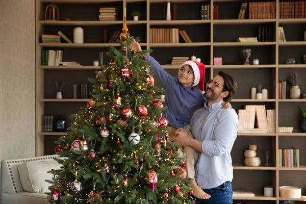Glücklicher junger Vater schmückt Baum mit kleinem Sohn. — Stockfoto