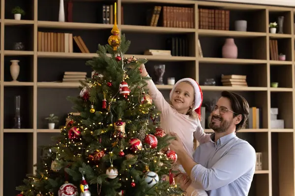 Liebevoller junger Vater schmückt Weihnachtsbaum mit Tochter. — Stockfoto