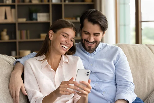 Glückliches junges Familienpaar nutzt Handy zu Hause. — Stockfoto