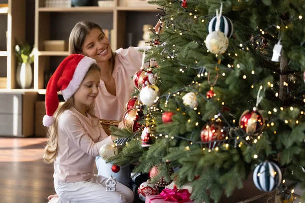 Glad liten barn dotter dekorera julgran med mamma. — Stockfoto
