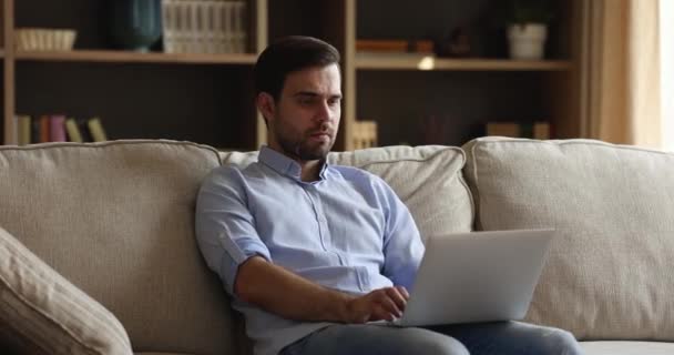 Συγκεντρωμένος νεαρός κάθεται σε καναπέ-laptop χρήση στη δουλειά — Αρχείο Βίντεο