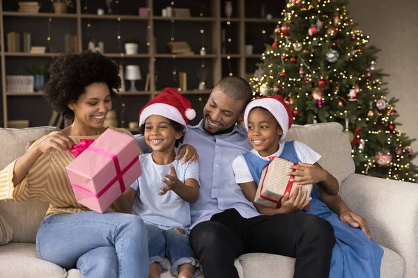 Sonrientes jóvenes afroamericanos padres desempacando regalos con niños. — Foto de Stock