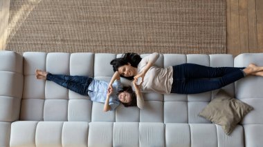 Mutlu genç Asyalı anne ve küçük oğlu kanepede yatıyor.