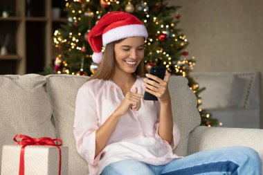 Noel Baba şapkalı mutlu kız akıllı telefondan yazı yazıyor.