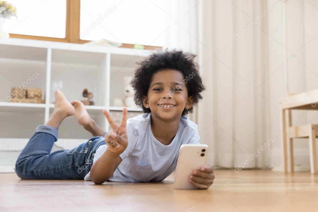 Joyful small child boy using cellphone alone at home.