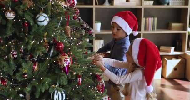 Küçük çocuk kız kardeşine Noel ağacını oyuncaklarla süslemesinde yardım et. — Stok video