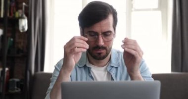 Adam dizüstü bilgisayarda çalışıyor. Gözlükleri çıkartıp göz ağrısını azaltıyor.