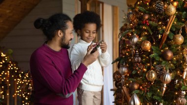 Çift ırklı baba ve oğulun bayrak manzarası Noel ağacını süslüyor