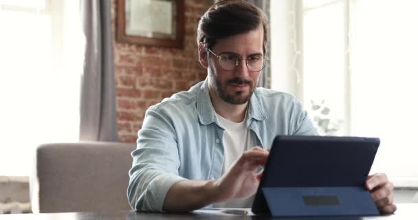 Seriöser Millennial-Mann sitzt mit digitalem Tablet am Tisch — Stockvideo